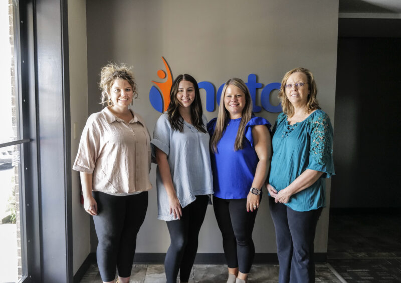 NCTC employees standing in front of NCTC logo in office building
